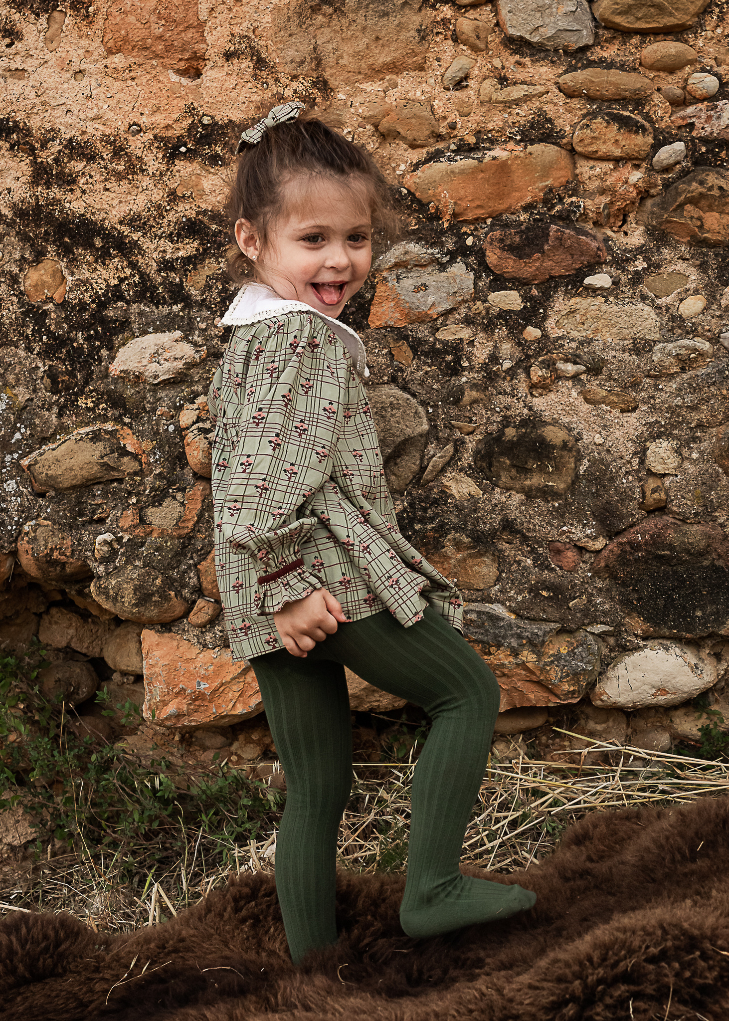 niña mostrando su vestido delante de un muro de piedra de una Masia en Pla de l'Estany en cataluña, españa.