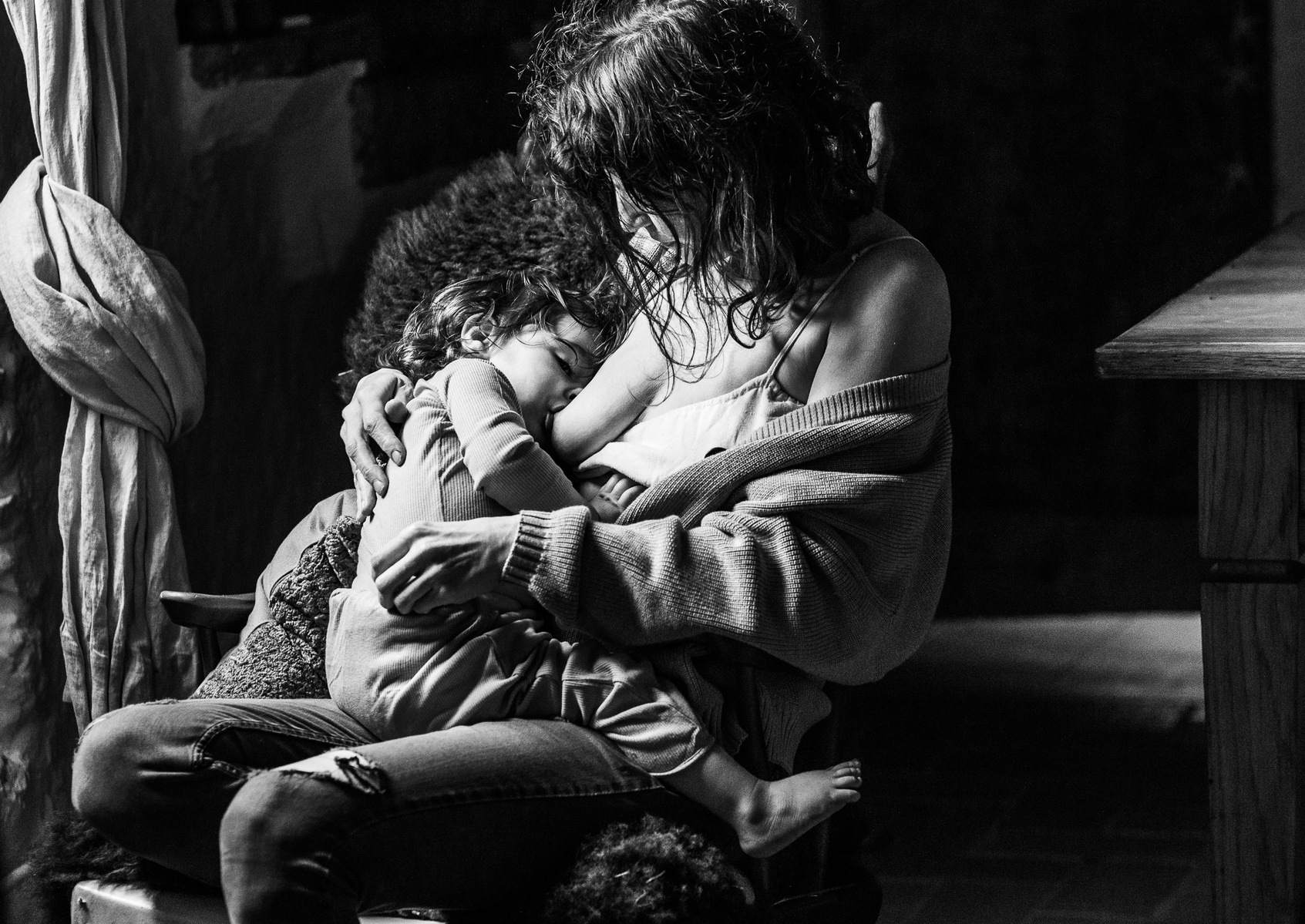 Madre amamantando a su bebe, en una silla, a la luz de una ventana en cataluña, españa