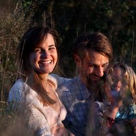 retrato de una familia con niña pequeña ella está embarazada  de 38 semanas, en los campos floridos de Pla de l'Estany, en girona, españa.