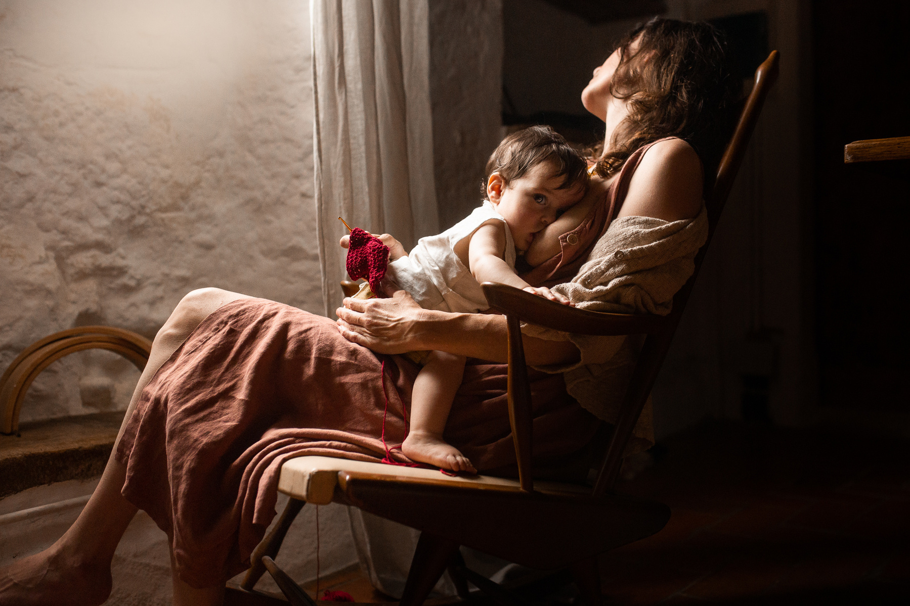 Madre reposando en una silla amamantando a su bebe, cerca de una ventana, plà del Estany, cataluña, españa