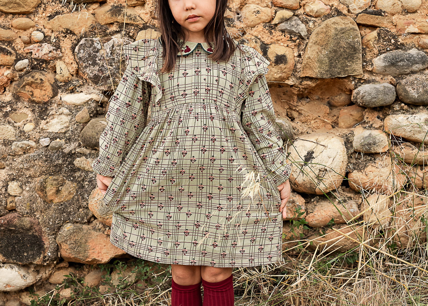 niña mostrando su vestido delante de un muro de piedra de una Masia en Pla de l'Estany en cataluña, españa.