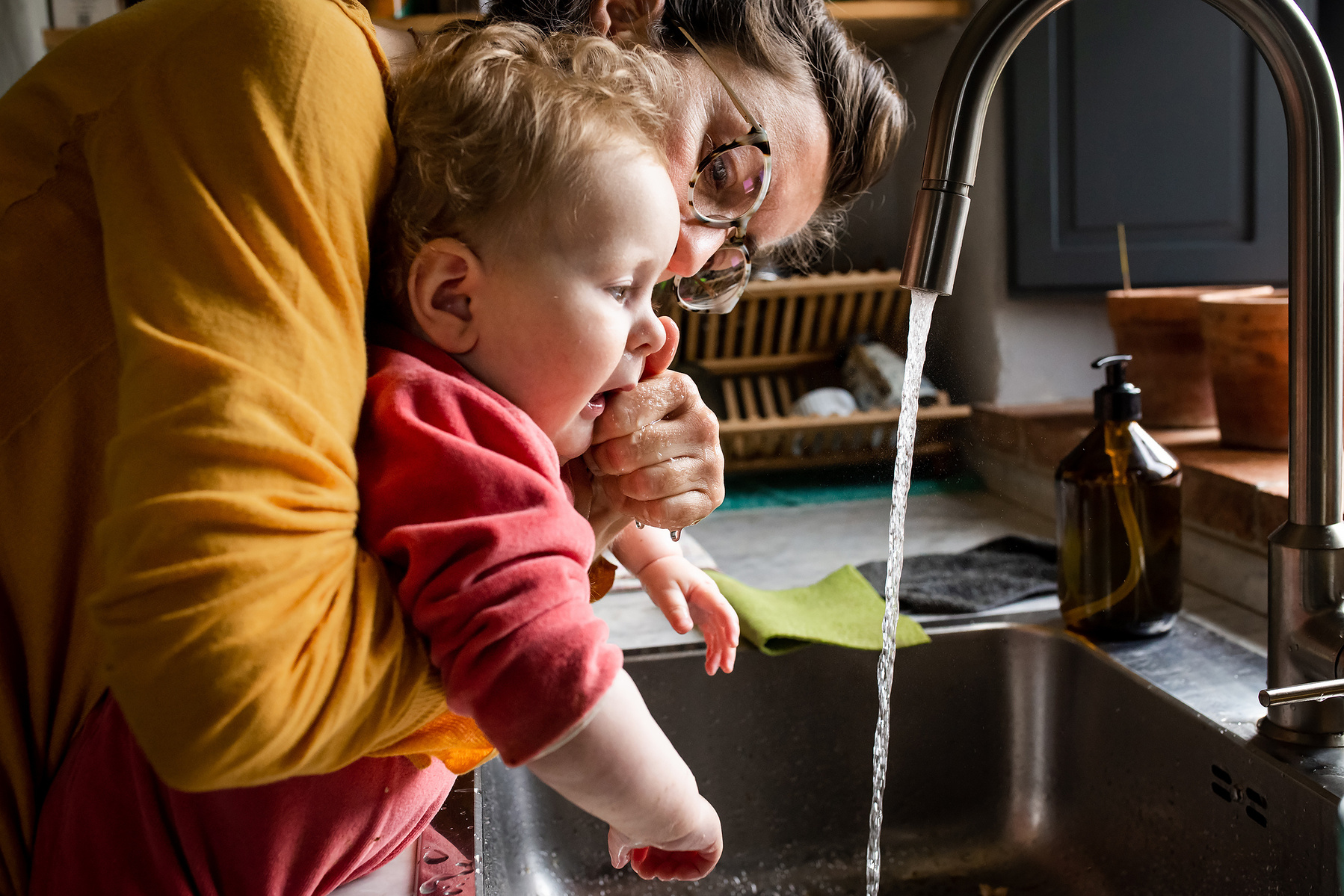 mamá limpiando la boca de su bebe en la pica de la cocina, fotografia de familia Manuela Franjou