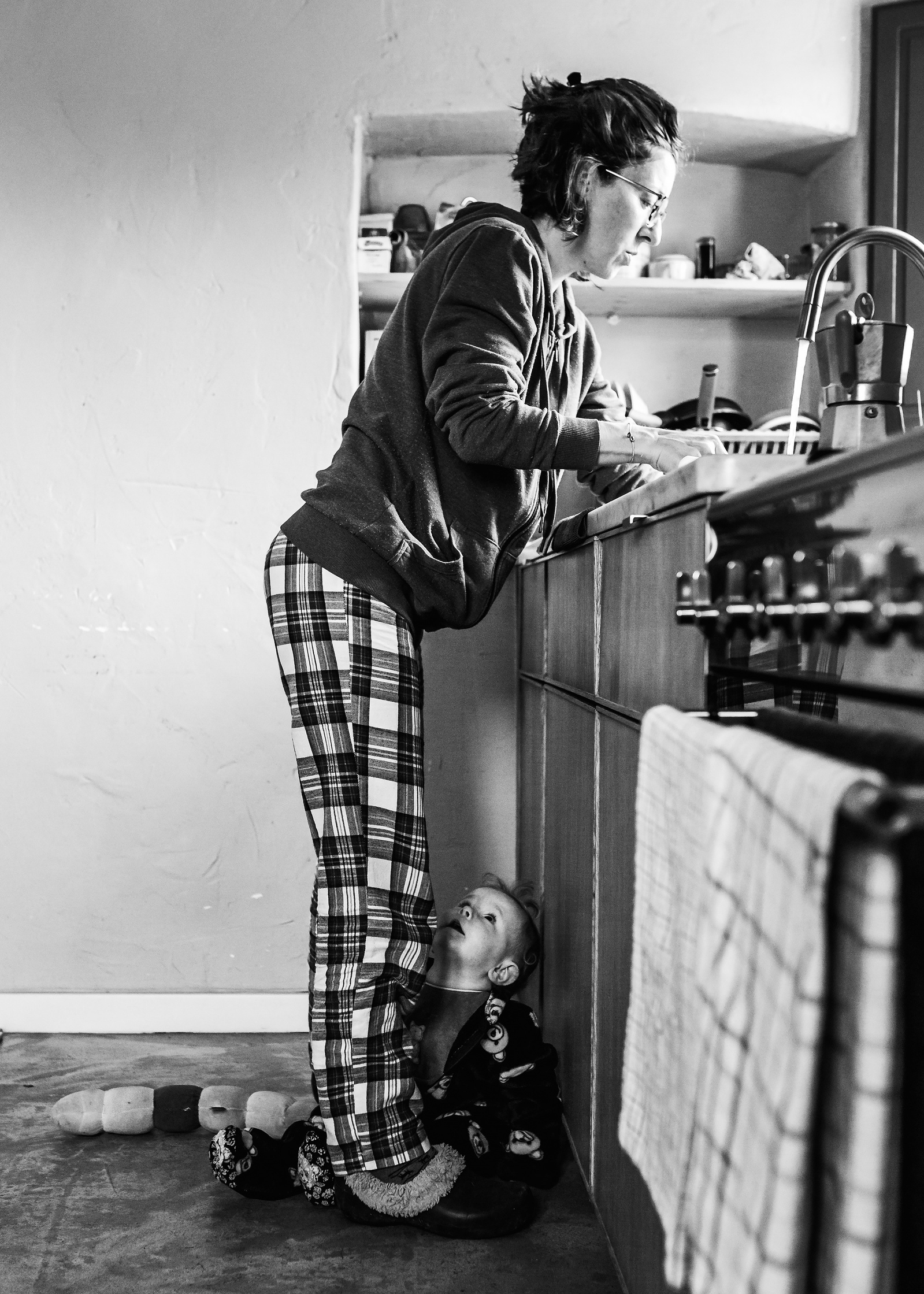 mamá limpiando en la pica de la cocina, bebé mirándola ,  fotografia de familia Manuela Franjou