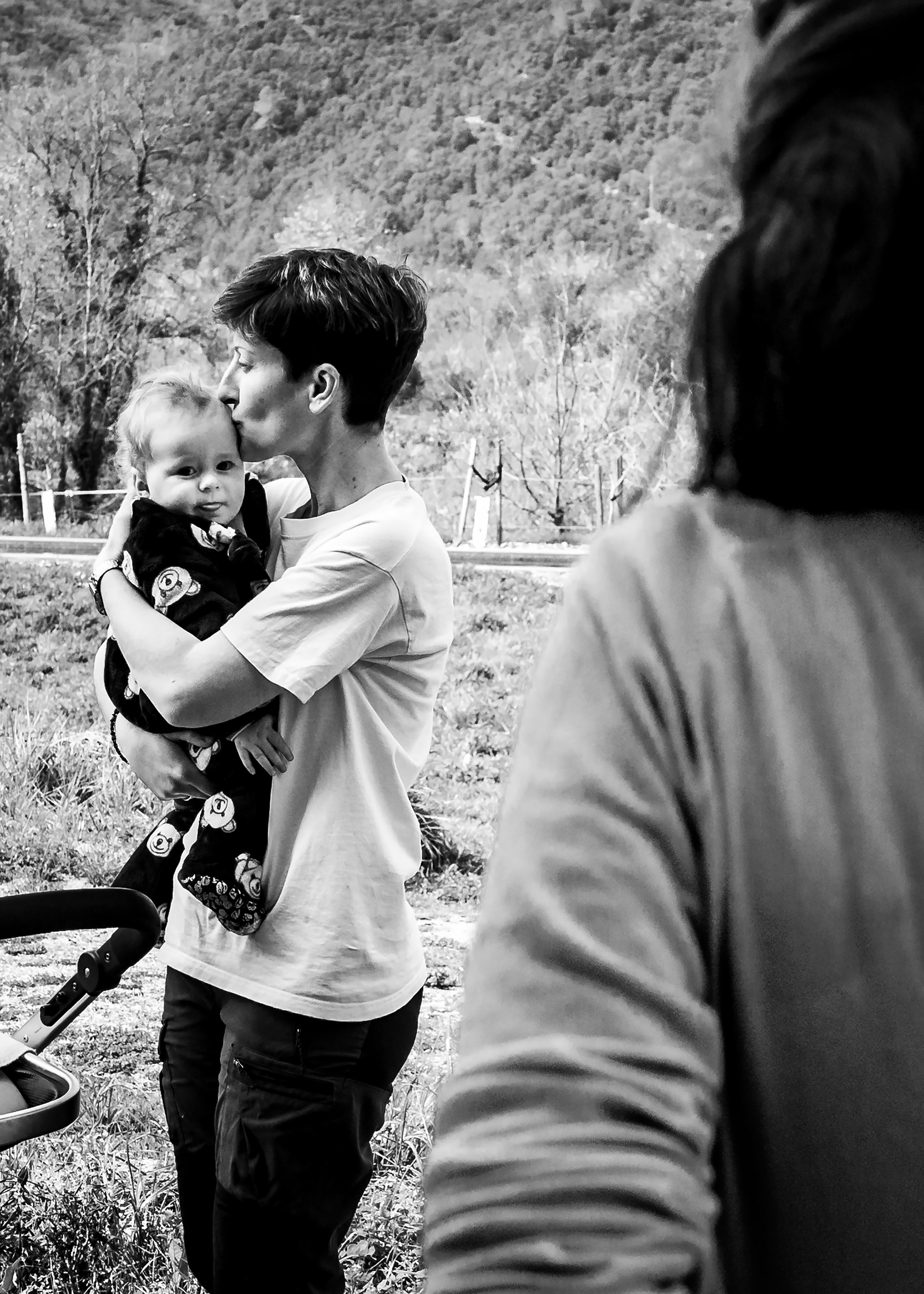 mamá besando su hijo bajo la mirada de otra mamá. Manuela Franjou fotografia de maternidad