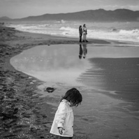 niño pequeño jugando en la playa y sus hermanos a lo lejos en la playa del Empordá
