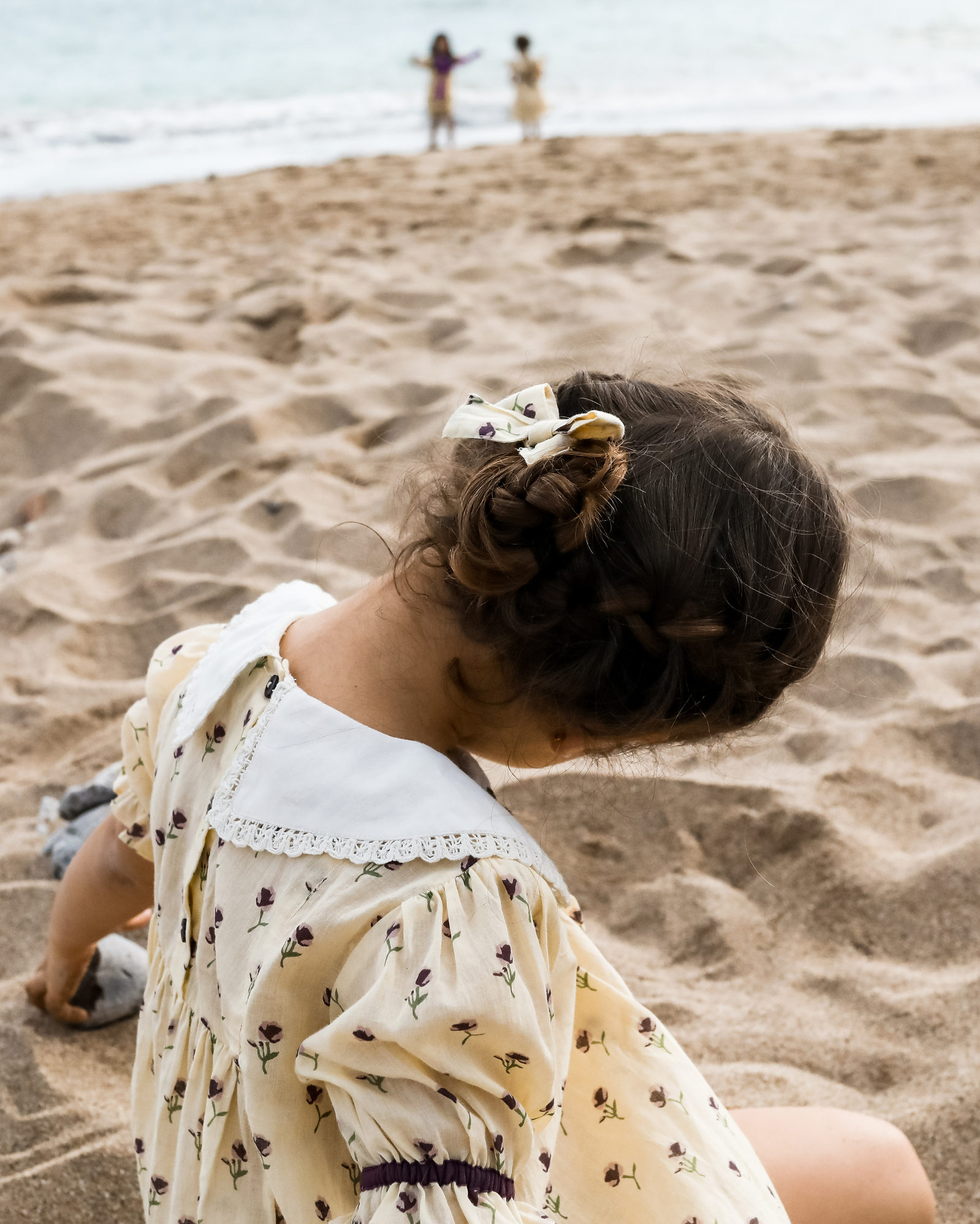niña jugando con la arena mientras sus amigas están cerca del mar en la playa de les casetas del Garraf en Barcelona, españa