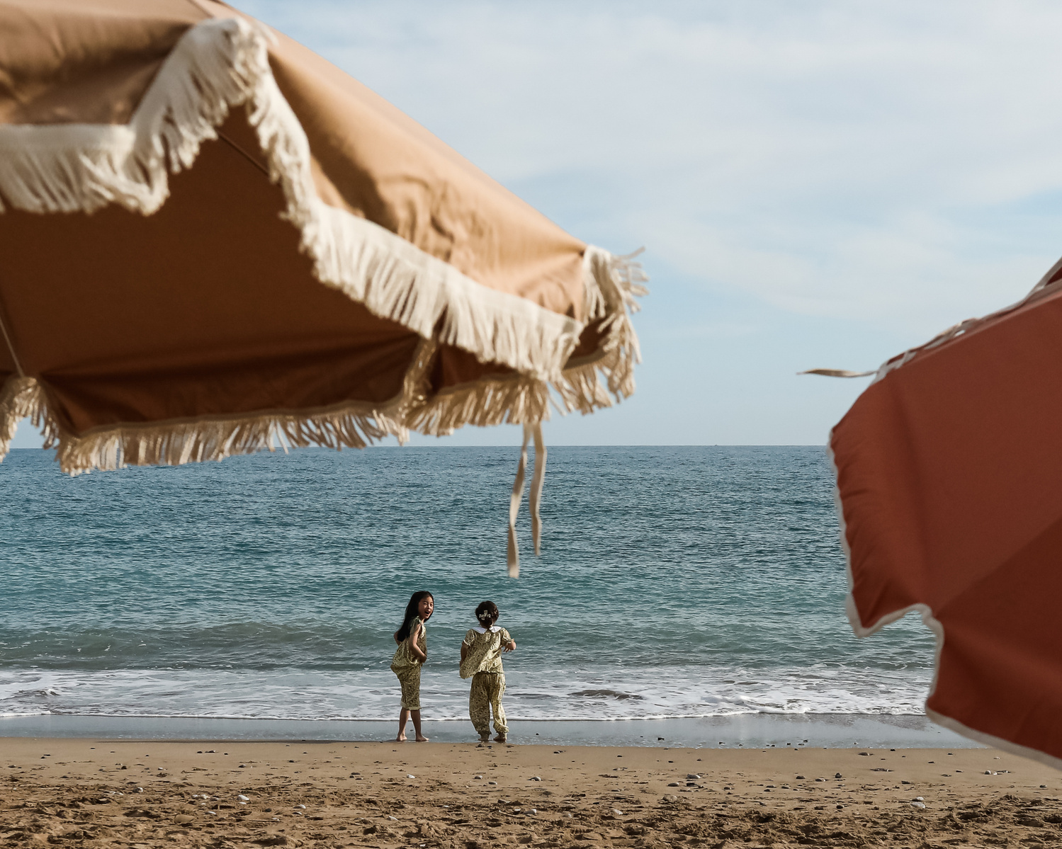 Dos niñas se ven a los lejos enmarcadas por una sombrilla en la playa del Garraf, barcelona spain.