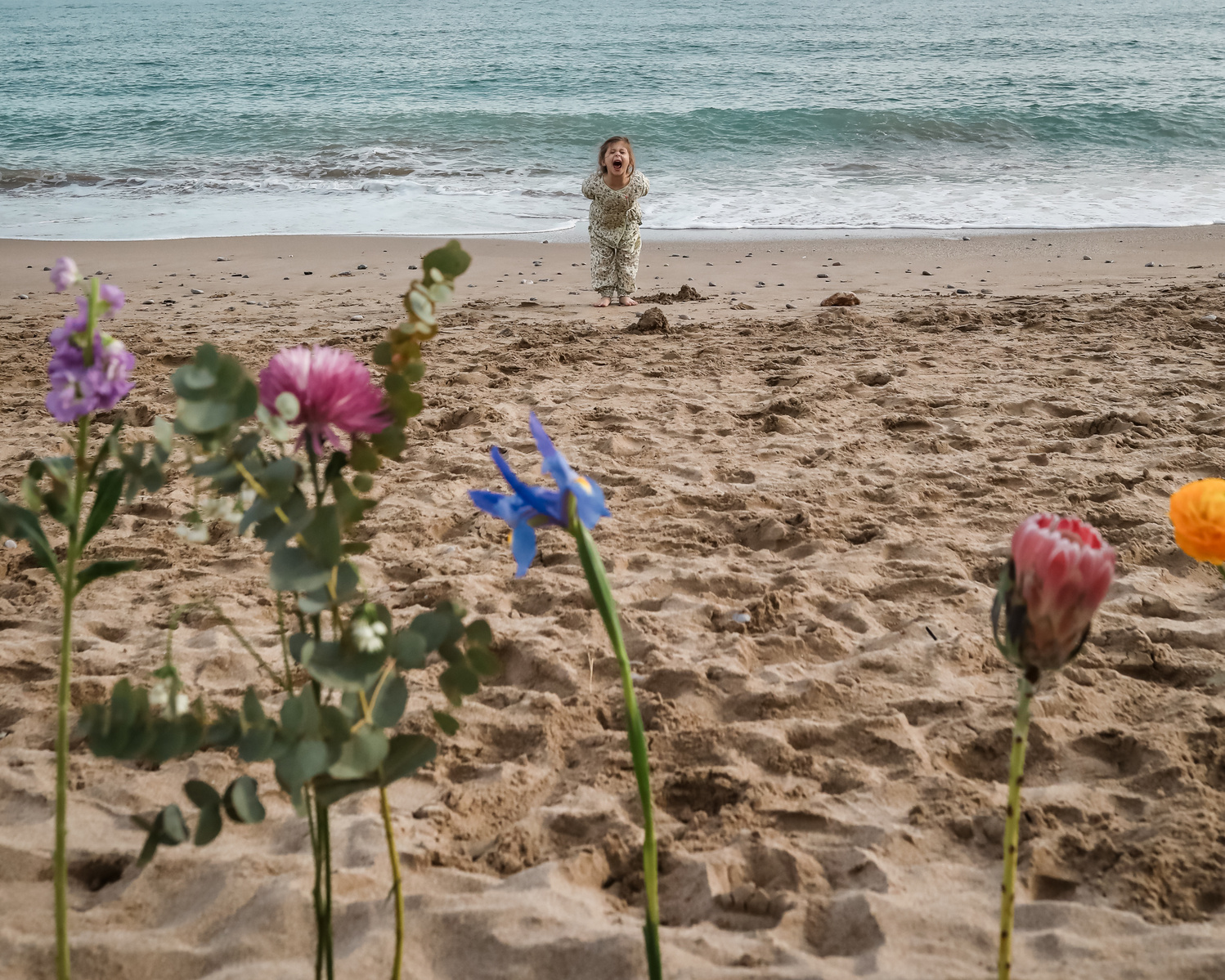 niña gritando con flores en primer plano en la playa las casetas del Garraf en barcelona, españa