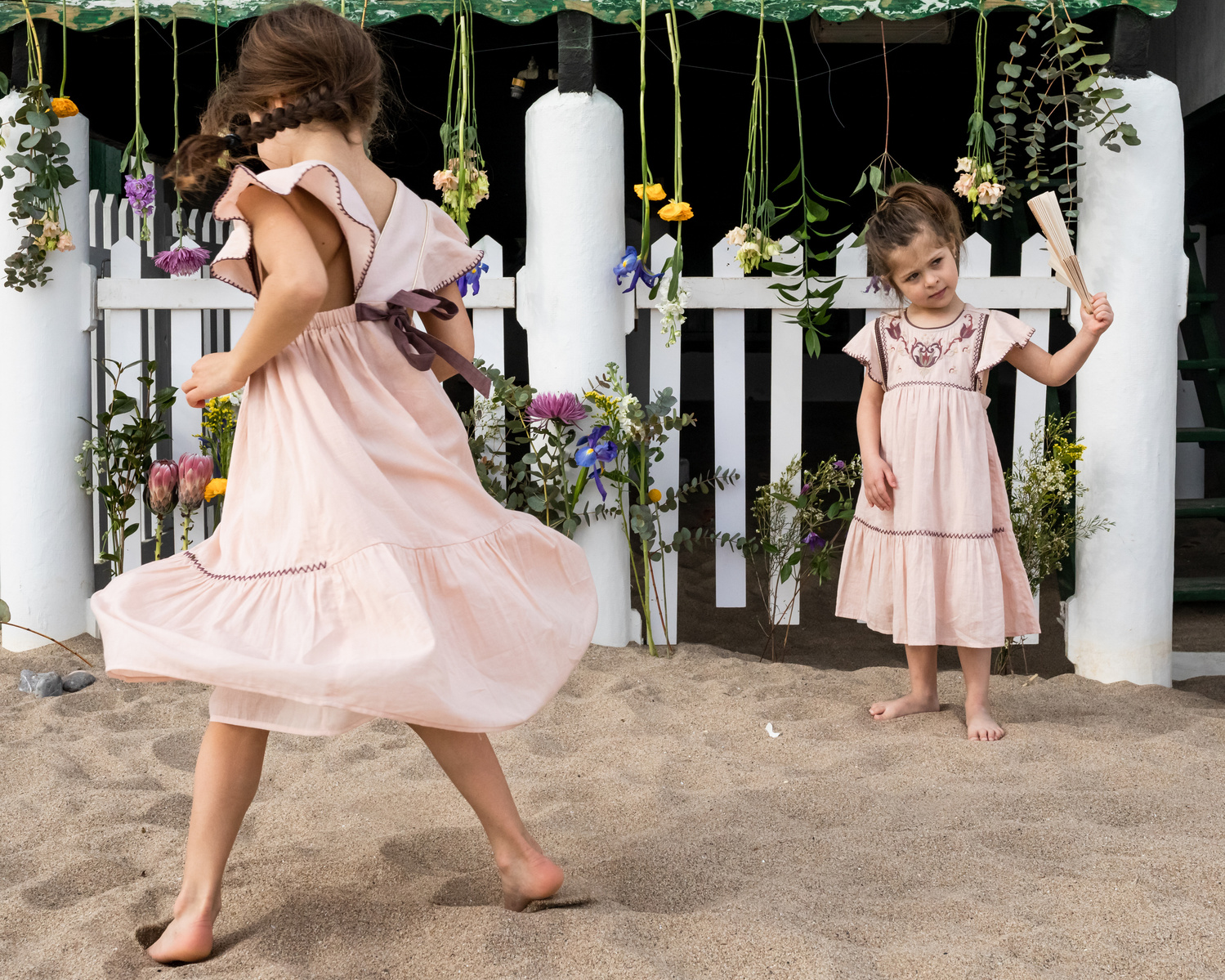 dos niñas, una da vueltas a su vestido en la playa las casetas del Garraf en barcelona, españa