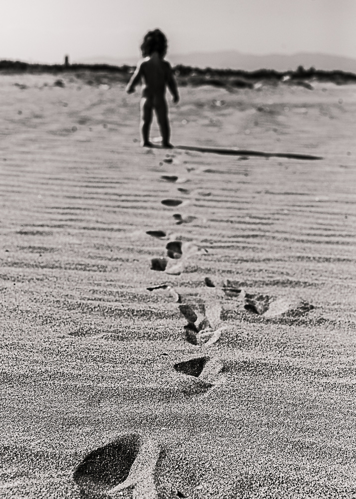 bebe dejando marcas de sus pasos por la arena, se ve su silueta en el fondo, en la playa de sant Pere pescador en alt Empordá, Catalunya, Spain 