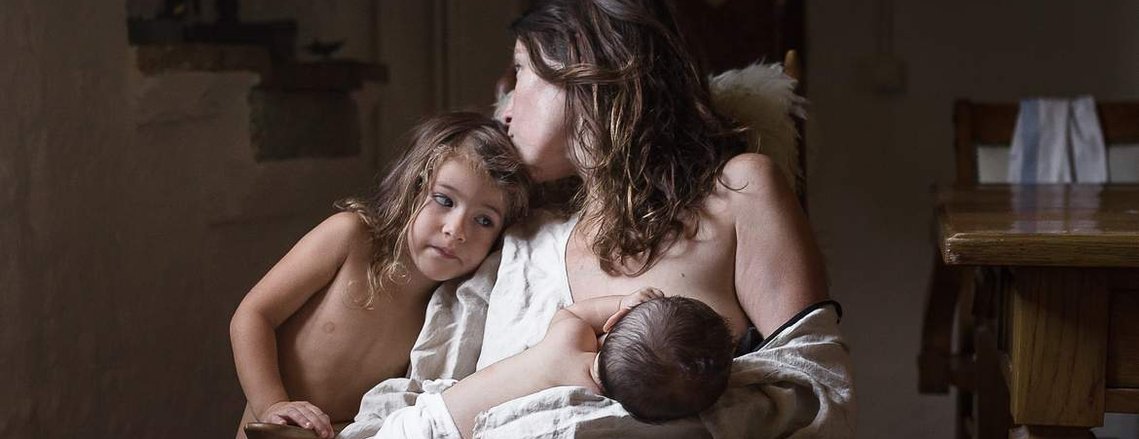 mother breastfeeding her baby and kissing her daughter, in an emotional way. Manuela Franjou, barcelona family photographer. 