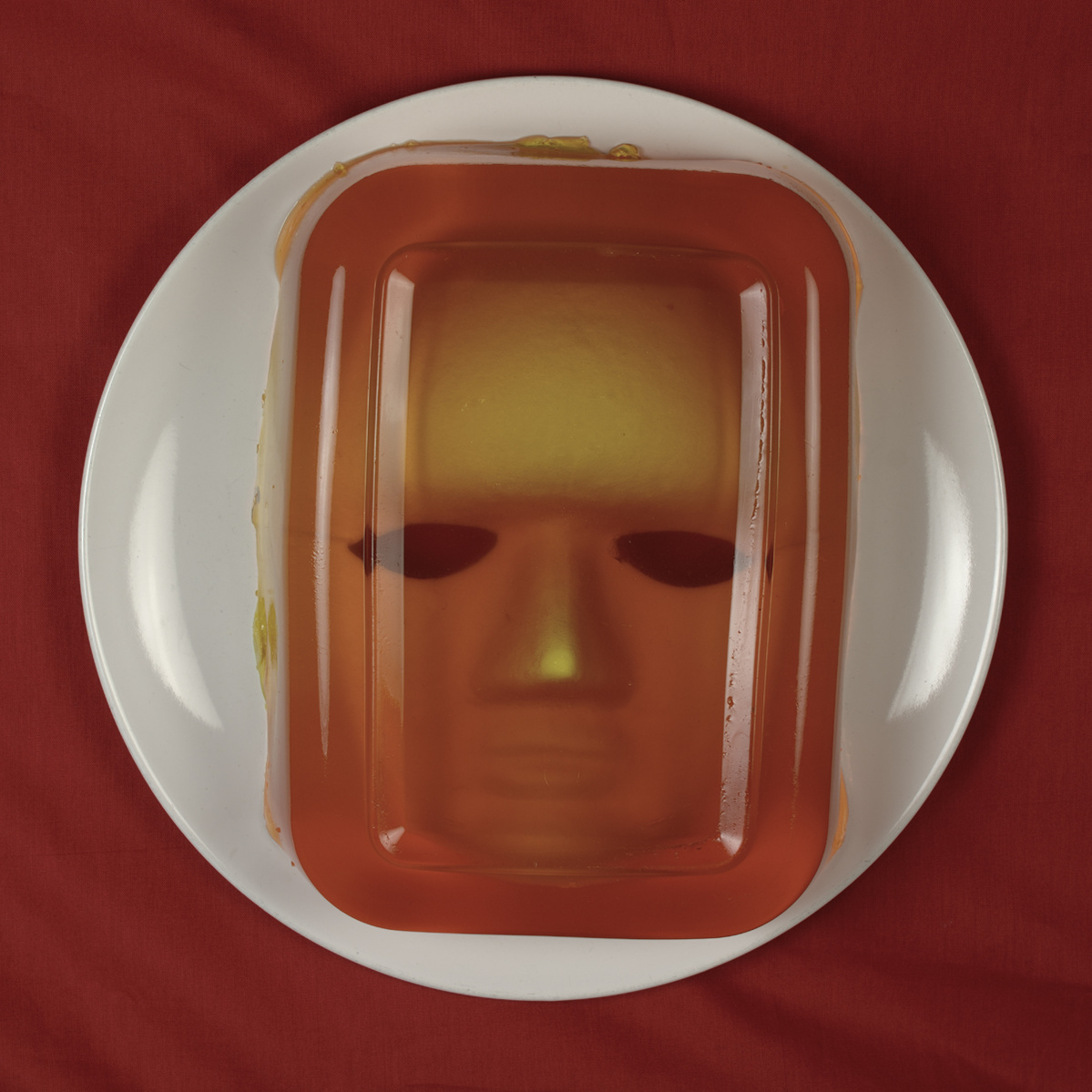 White plate with face peering through orange jelly