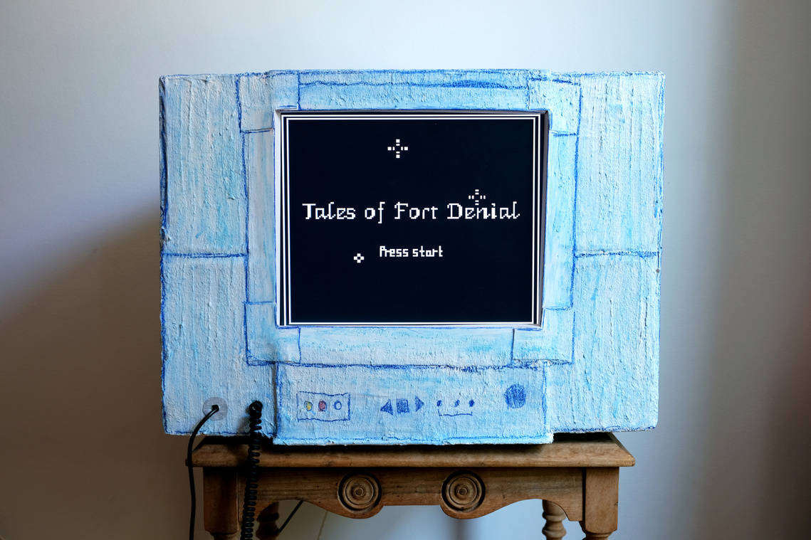 A blue paper mache tv playing a fantasy video game title screen that reads Tales of Fort Denial