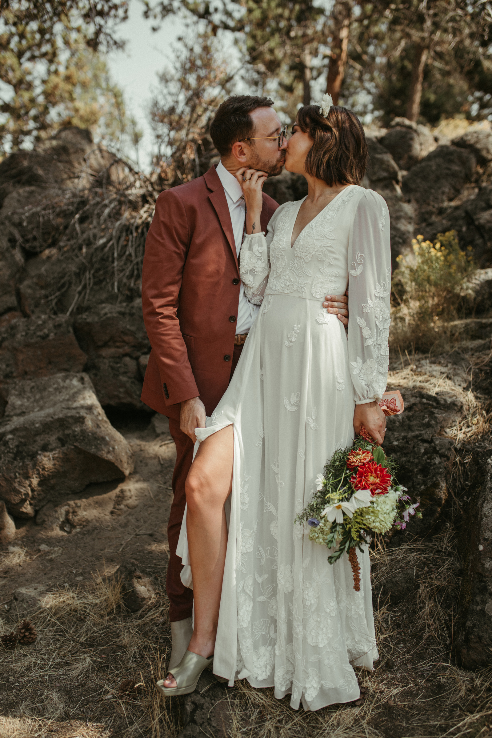 A stylish couple in thrifted wedding outfits kiss in Ben Oregon in the woods on their wedding day in the Summer