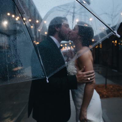 A couple in love kissing underneath an umbrella in the rain on their wedding day in St. Paul Minnesota.