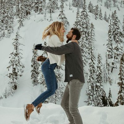 A couple jumps and tackles each other in the snow on Mount Baker for their engagement photos. 