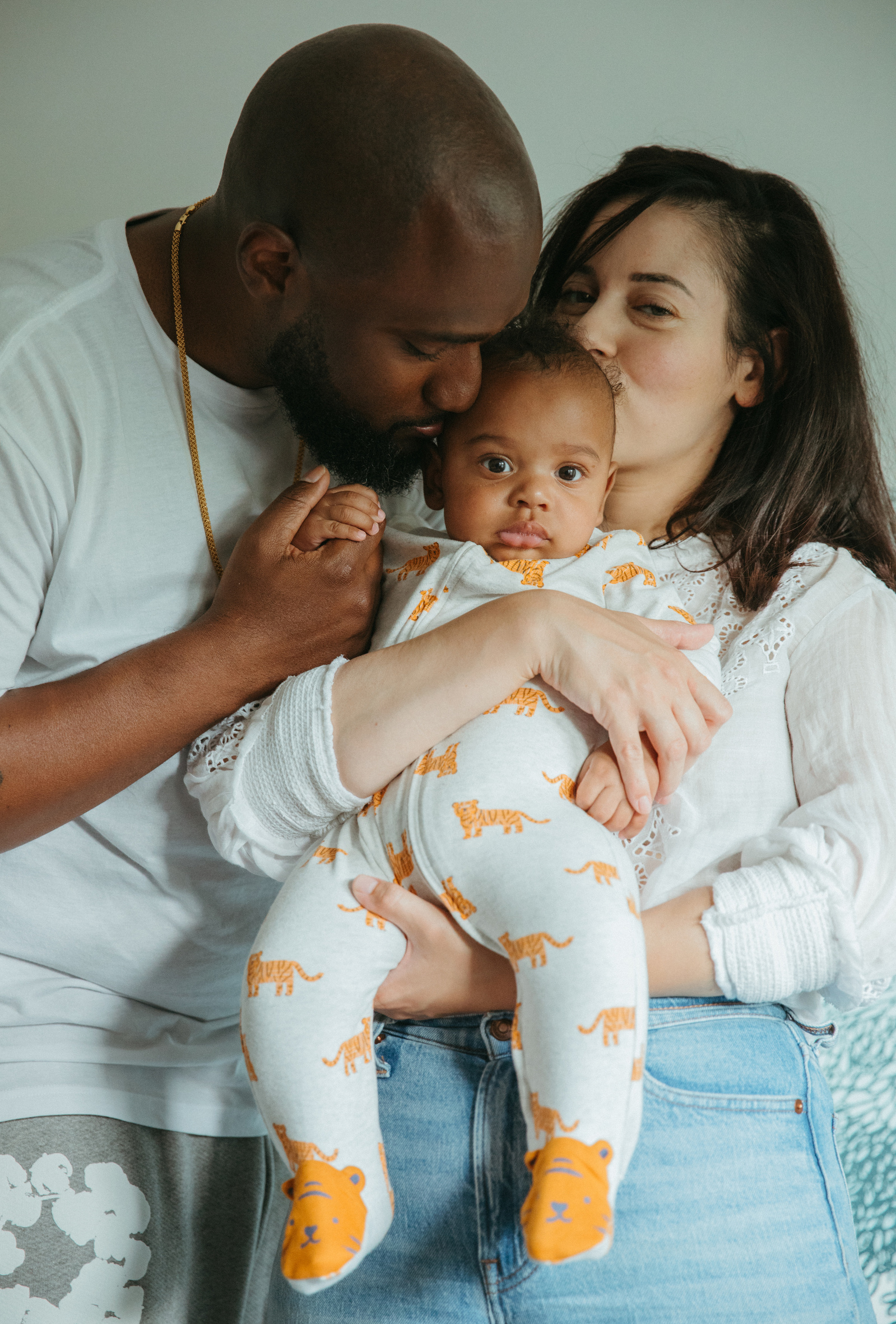 A sweet family poses together and kisses their newborn baby during their family photoshoot in St. Paul MN,