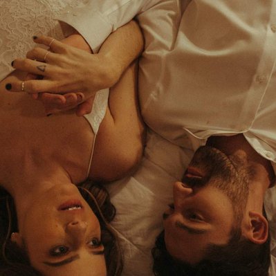 A coupe snuggles in bed holding hands shot on moody film after their wedding day. 