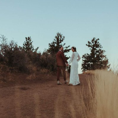 A couple in their wedding outfits walking through the high desert fields of Bend Oregon underneath the moon on their wedding day.