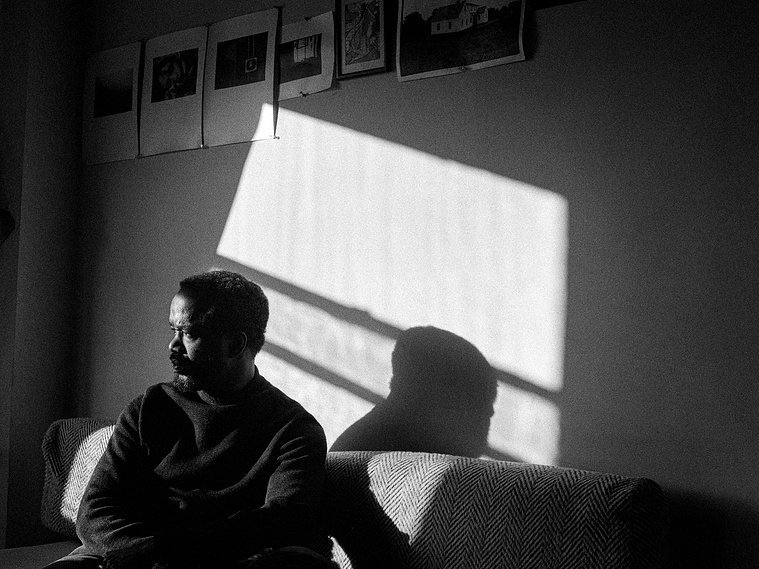 Self-portrait of James O. Mitchell sitting on a couch, sidelight casting his  shadow in patch of sunlight on the wall behind him 