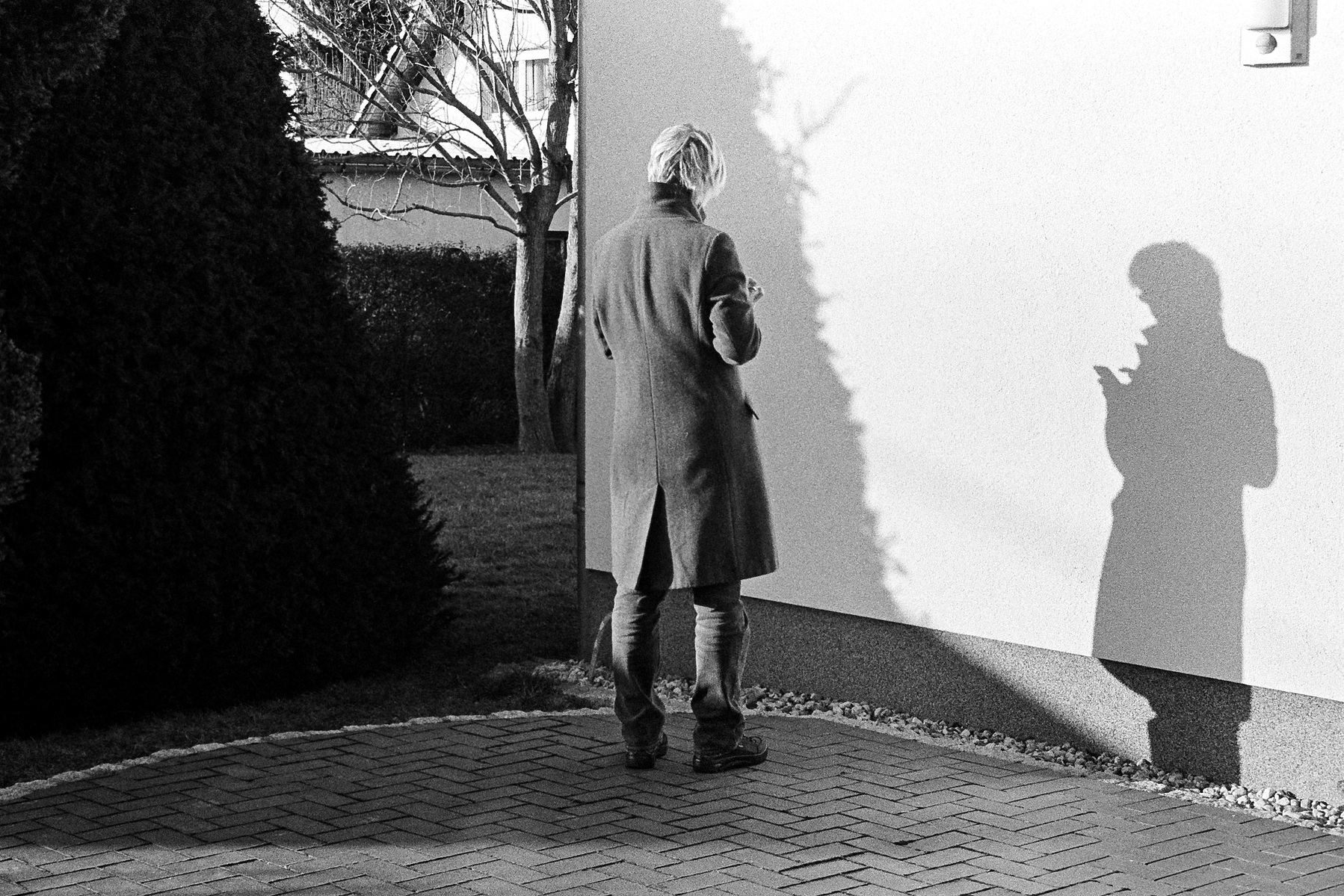 Black and white photo of a woman standing in the sun. The shadow of her body creates a silhouette on a white wall. Ilford HP5 plus 35 mm film.