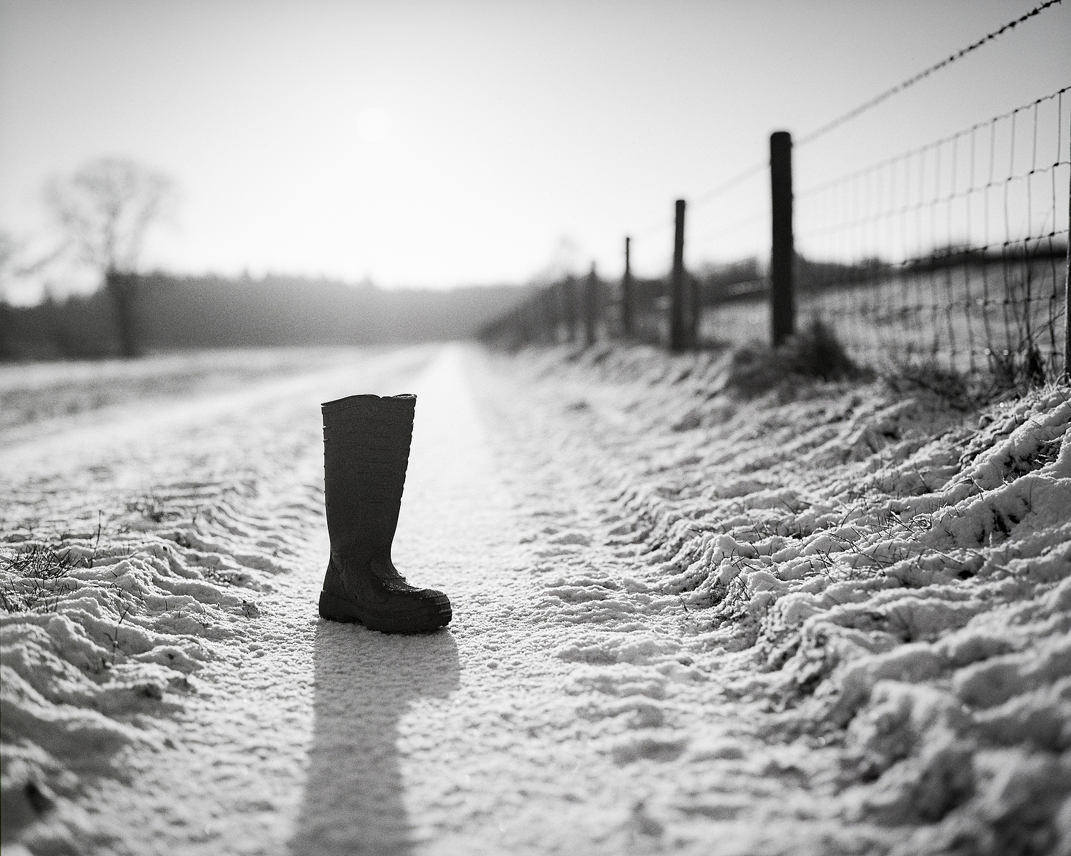 Photo of a single rubber boot on a snowy trail throwing a long shadow. Shot on Ilford Pan F plus medium format film.