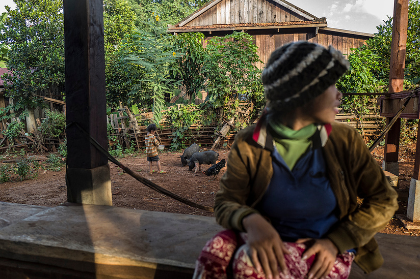 Kang Pisey - 22 sits whilst her son Bunthoeun Saroeun (3) feeds pigs and chickens at he family home in Charoung Commune - O Chum District, Ratanakiri Province, Cambodia.