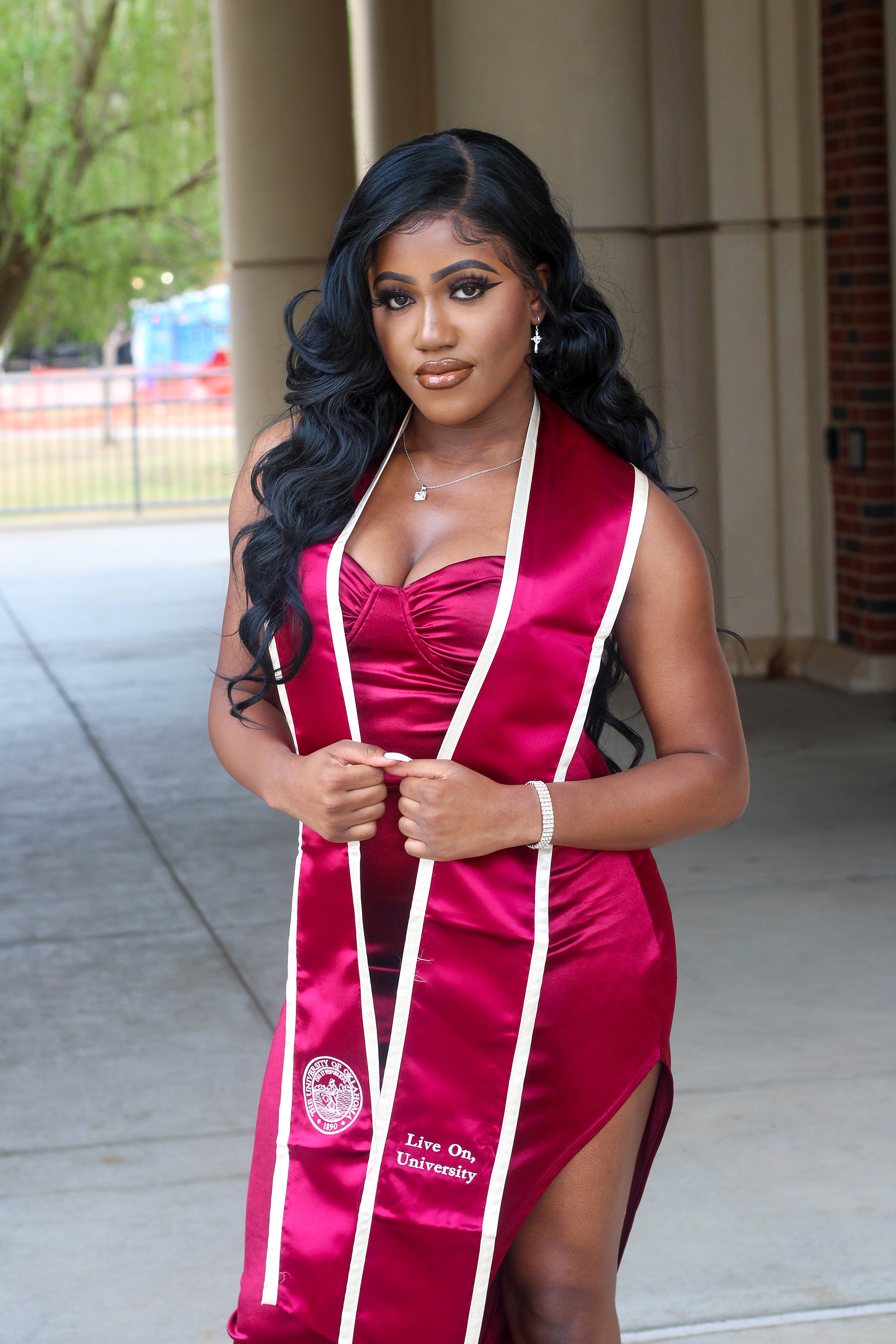 A stunning graduate in a burgundy satin dress and matching stole proudly poses at the University of Oklahoma. Her confident expression and elegant gown highlight the excitement of this milestone.