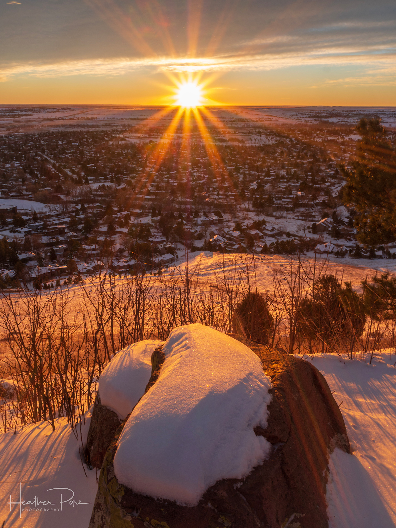 winter sunrise over boulder, colorado as the sun creates a sun star over the snow covered landscape