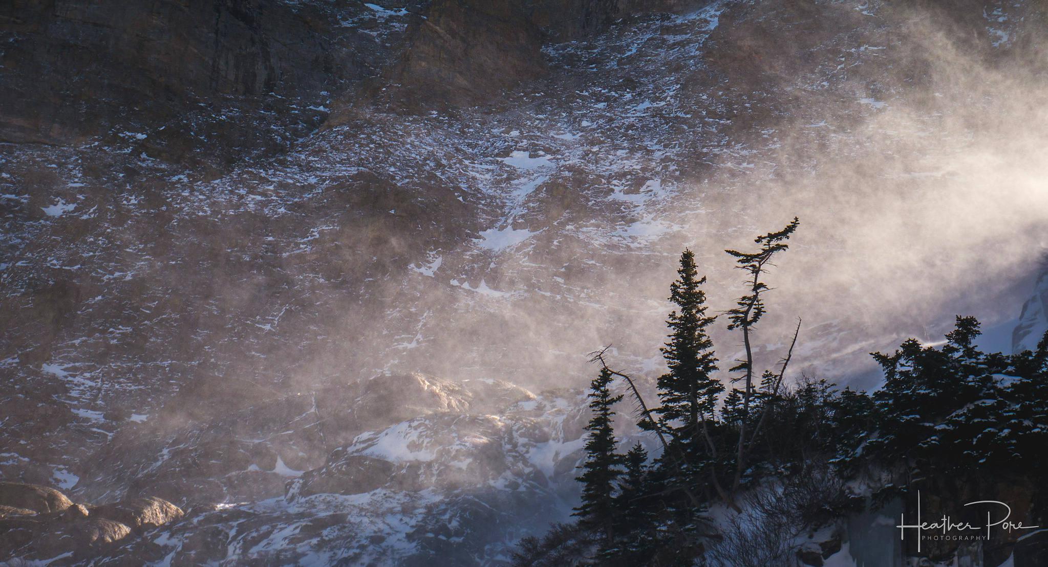 intimate landscape photograph of sunlight filtering through blowing snow in the mountains