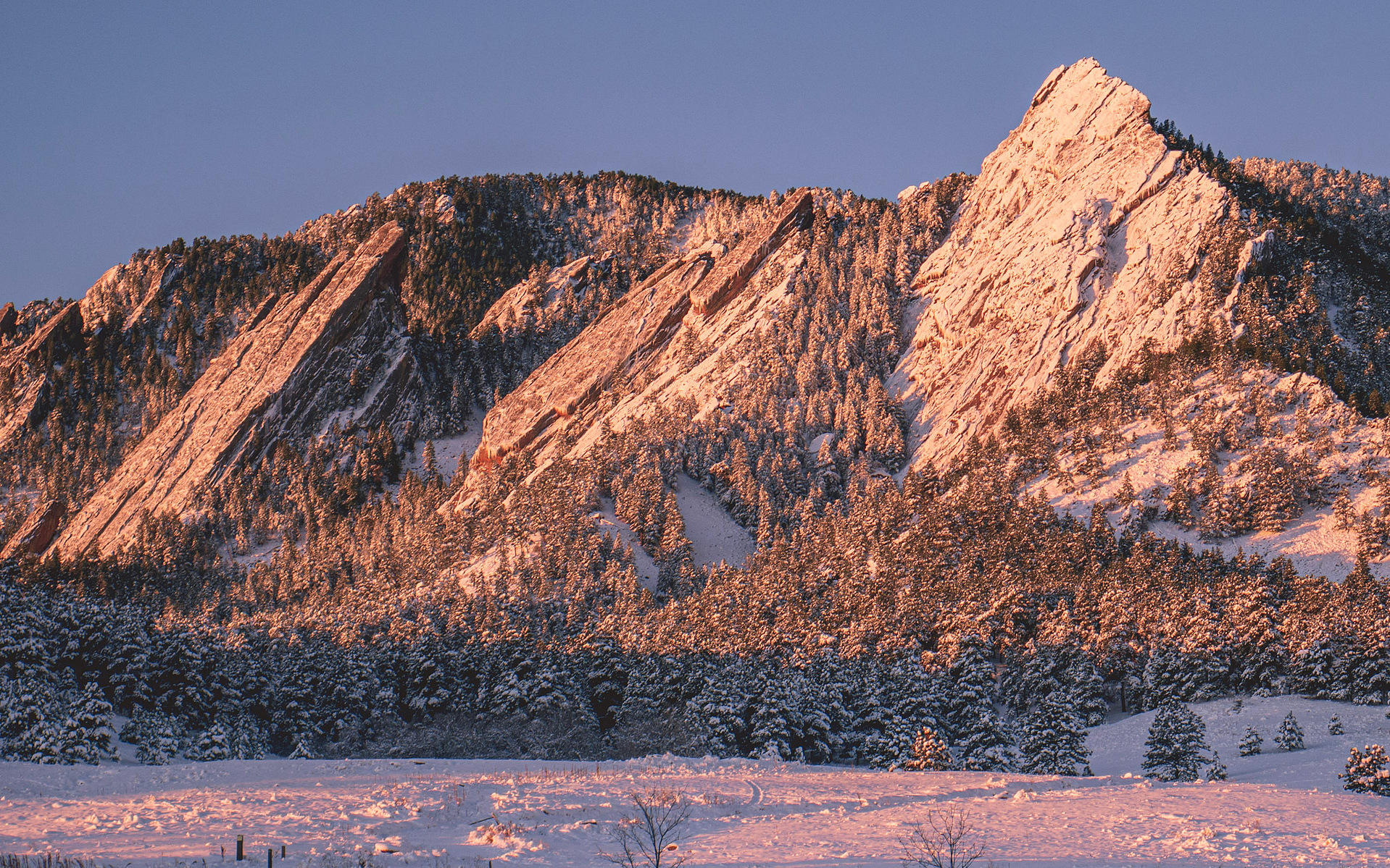 golden sunrise light shining on the snow covered flatirons in boulder, co