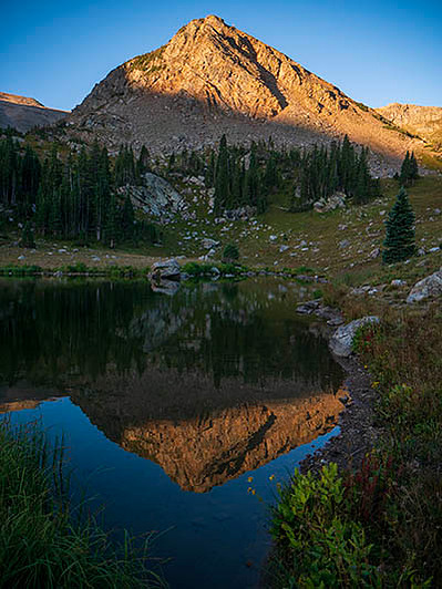 sunrise light hitting haystack mountain in james peak wilderness, reflecting in a small lake below