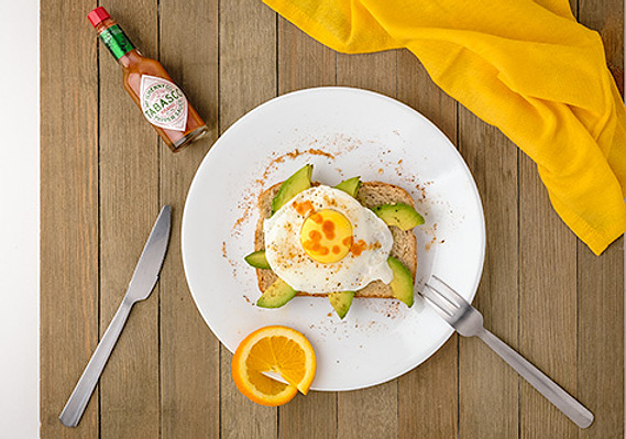 Image of avocado toast on a place setting with featured product. Shot in studio with soft lighting, well-suited for menus, social media posts, or a web site.