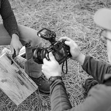 Woman whittling wood, while photographer takes close up shot, in lifestyle product photo. 