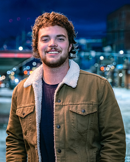 Young man in fleece lined jacket on city streets at night. Ambient and natural lighting. Great environmental portrait.