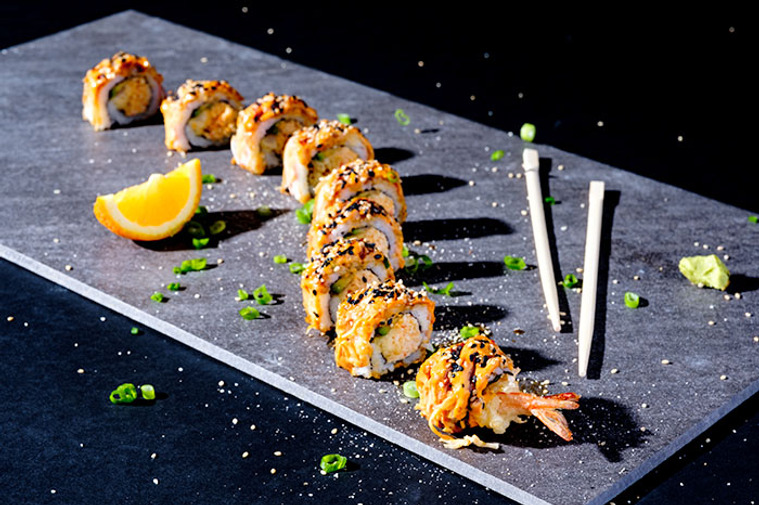 Sushi roll in snaking pattern served on slate  in harsh light. Great, modern food photo with advanced lighting.