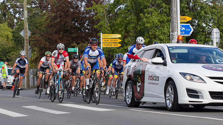 Group of male cyclists' starting a bike race with car in front and spectators' watching