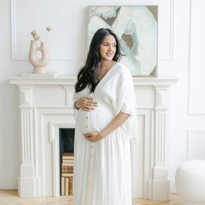 Pregnant woman holding wearing a white and standing in front of fireplace
