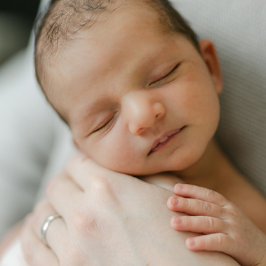Newborn baby sleeping with his hand resting on his dad's hand
