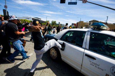A protester kicks a LAPD patrol car rushing to another part of the district.