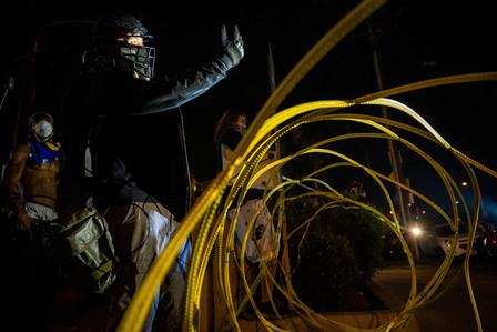A protester in black bloc challenges Los Angeles County sheriff's deputies to cross the wire metal barricade by the sheriff's station in South Los Angeles and fight him, Monday, Sept. 7, 2020.