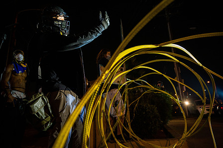 A protester in black bloc challenges Los Angeles County sheriff's deputies to cross the wire metal barricade by the sheriff's station in South Los Angeles and fight him, Monday, Sept. 7, 2020.