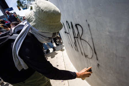 A masked protester tags the wall with "ACAB!", an acronym for "All cops are bastards."