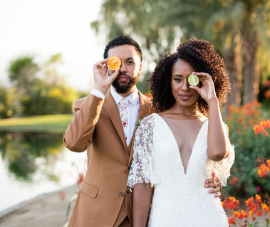 Bride and Groom in Palm Springs with citrus fruit covering one eye for an editorial wedding shoot.