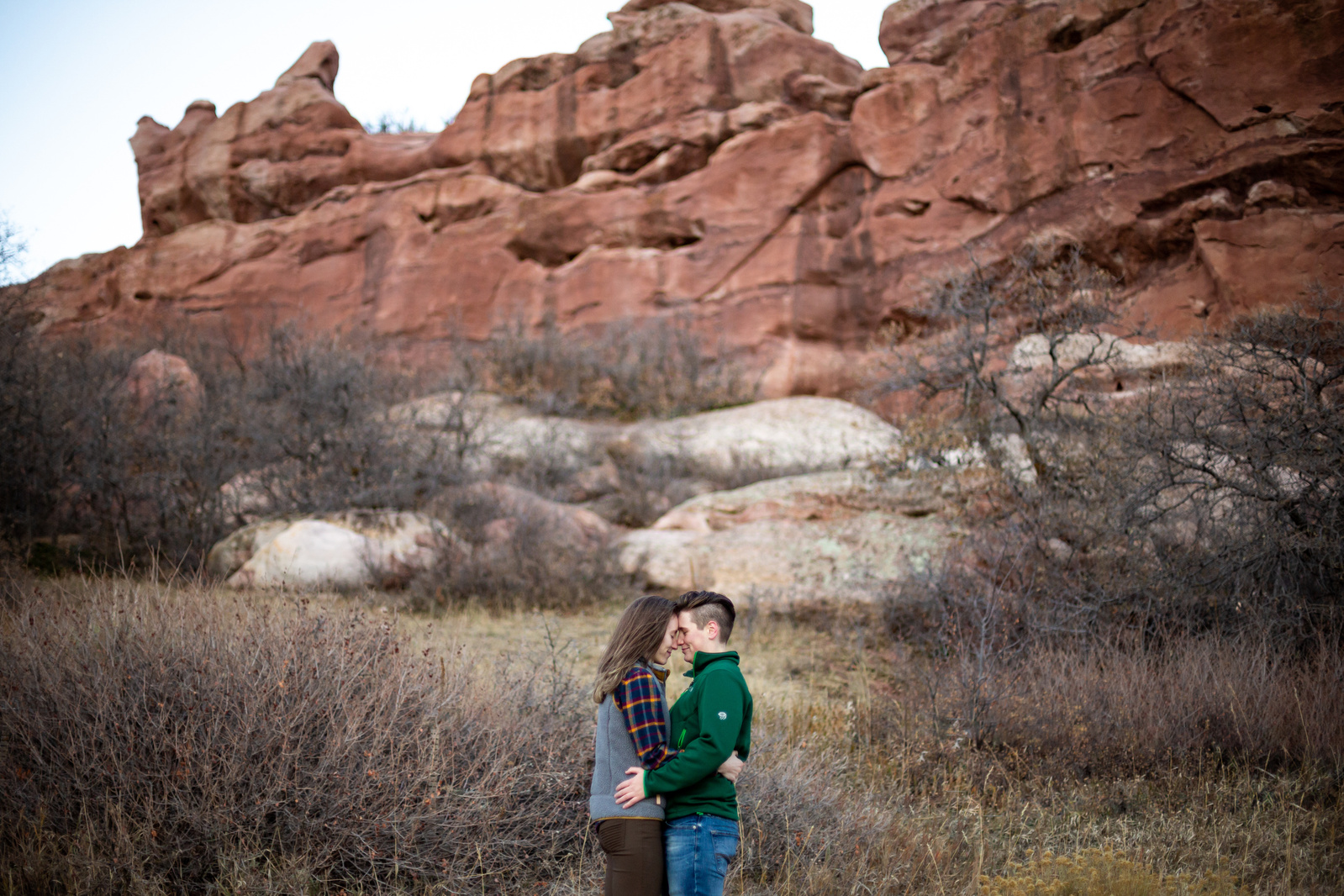 Two women kissing in front of red rock sandstone in South Valley Park in Littleton, Colorado. Engagement photography session with Simone Schiess Photography, Denver Wedding Photographer
