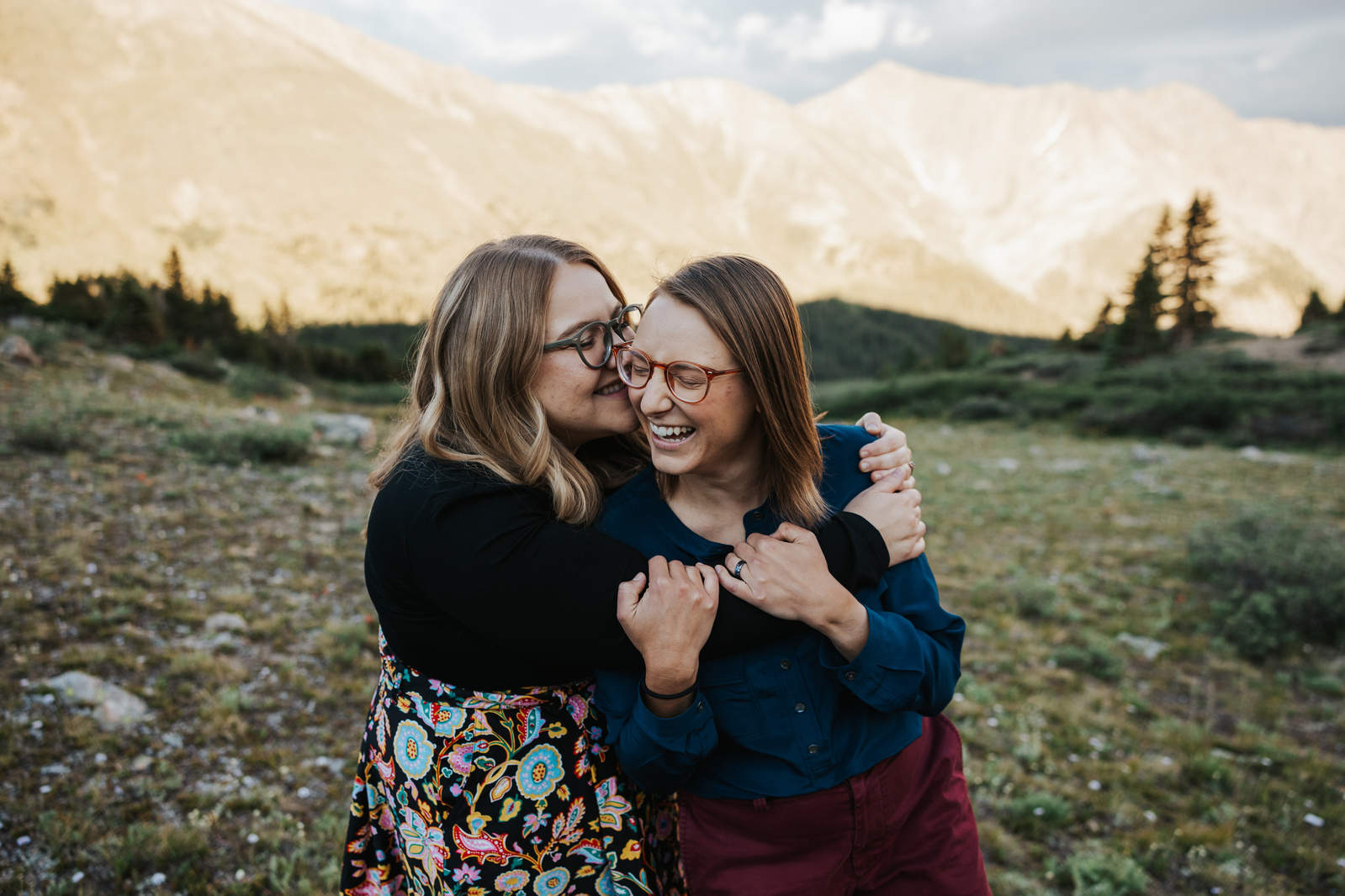 Two women hugging and laughing on top of a mountain at sunset in Colorado during an engagement photoshoot with Simone Schiess photography. 