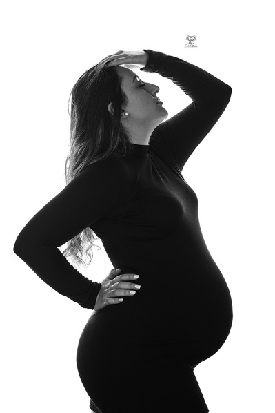 Chica embarazada posando mirando hacia arriba con una mano apoyada en la frente. Fotografia profesional