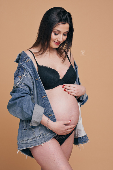 Chica embarazada posando mirando hacia la barriga con las manos apoyadas  por arriba y por abajo de la barriga. Fotografia profesional