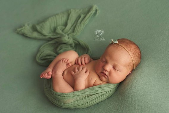 Recien nacido durmiendo con diadema sobre sabana verde 