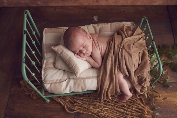 Recien nacido durmiendo con la mejilla apoyada en las manos sobre  en una camita de forja estilo vintage en suelo de madera